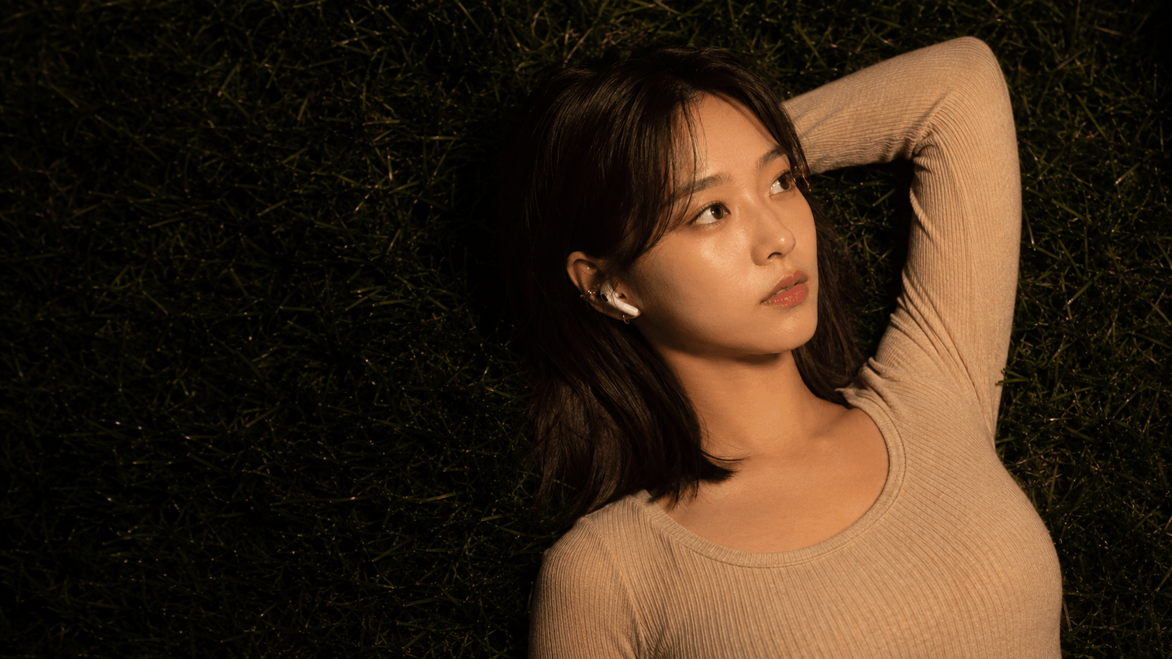 Mia lies in the grass at night with one arm behind her head, listening through her earbuds.